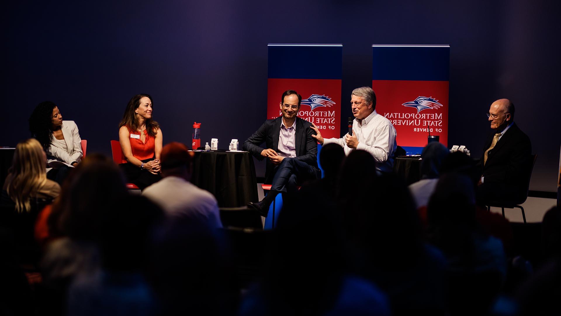 L to R, David Fine, Wayne Williams, Phil Weiser, Janine Davidson and Katia Campbell sitting on a panel in the CAVEA space on campus